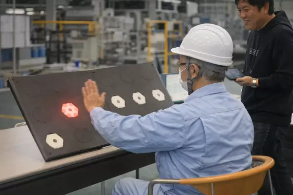 工場でヘルメットを着用した作業員が、光るデバイスに手を伸ばして反応を測定している様子