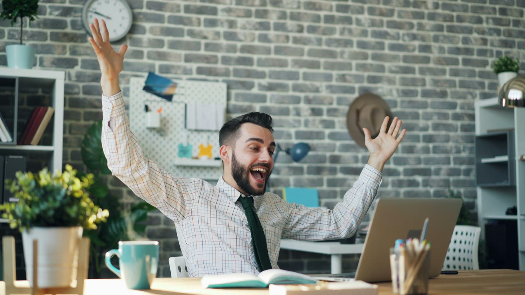 オフィスのデスクで両手を挙げて喜ぶ会社員